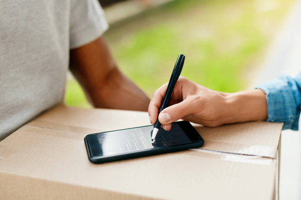 Package Delivery. Close Up Hand Signing On Phone On Box - Foto, afbeelding