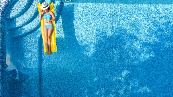 Девочка отдыхает в бассейне, плавает на надувной матрасе и веселится в воде на семейном отдыхе, на курорте, сверху открывается вид на воздушный дрон
 - Фото, изображение