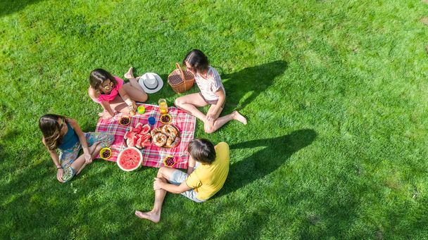 Happy family having picnic in park, parents with kids sitting on grass and eating healthy meals outdoors, aerial view from above, family vacation and weekend concept - Foto, Imagem
