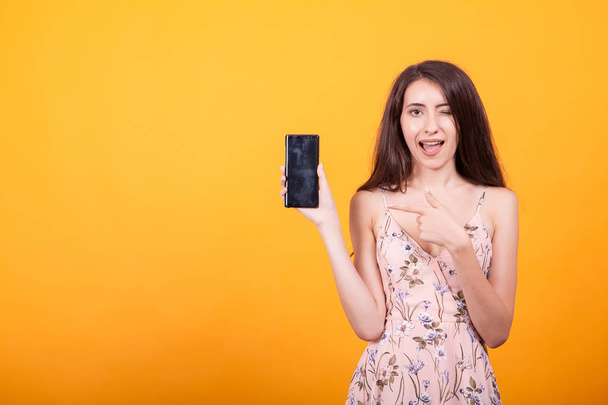 carino giovane donna che punta sul suo telefono in studio su sfondo giallo
 - Foto, immagini