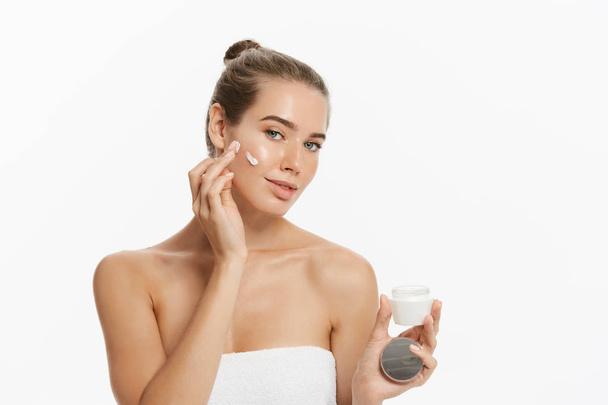Όμορφη νεαρή γυναίκα εφαρμογή καλλυντικά θεραπεία κρέμα στο πρόσωπό της, απομονώνονται σε λευκό φόντο - Φωτογραφία, εικόνα