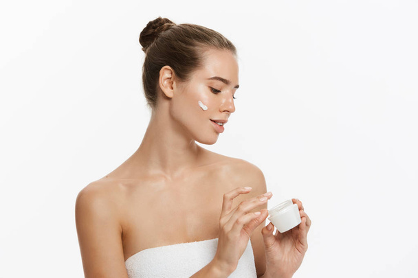 schöne junge Frau Anwendung kosmetischer Creme Behandlung auf ihrem Gesicht isoliert auf weißem Hintergrund - Foto, Bild