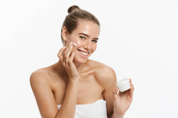 Gyönyörű fiatal nő, kozmetikai krém kezelés alkalmazása az arcán, elszigetelt fehér background - Fotó, kép