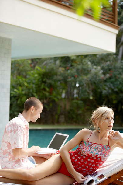 Sophisticated couple relaxing by the swimming pool of their holiday home garden - Fotoğraf, Görsel