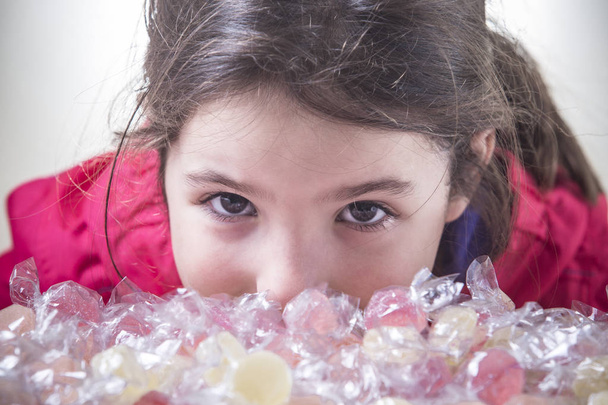 Dziecko dziewczynka wyglądają na aparat za dużo gummies zawinięty jelly miękkim. Zbliżenie - Zdjęcie, obraz
