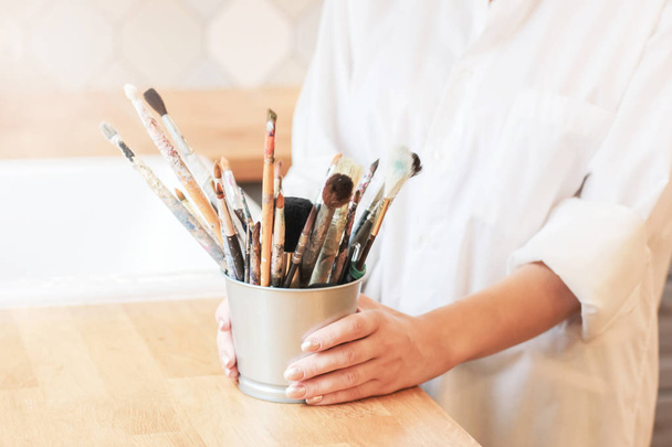 Different brushes in metal bucket with artist hands, selective focus - Photo, Image