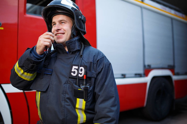 Photo of smiling fireman talking on walkie-talkie with fire engine - Foto, Bild