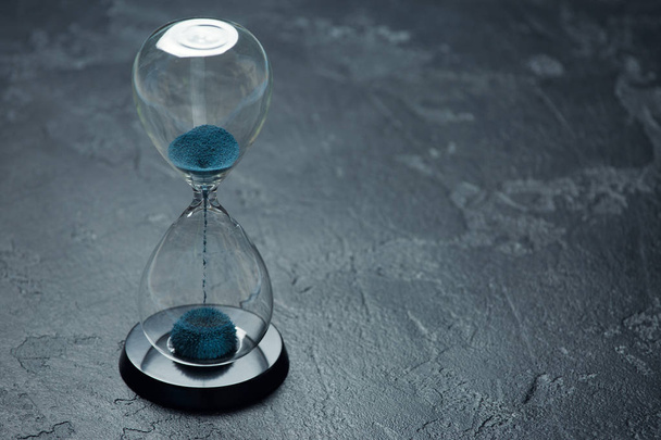 Image of hourglass with blue sand on black background - Photo, Image
