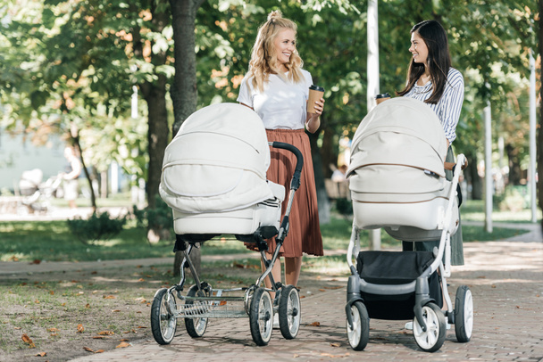 Mütter mit Kaffee zum Gehen und Spazierengehen mit Kinderwagen im Park - Foto, Bild