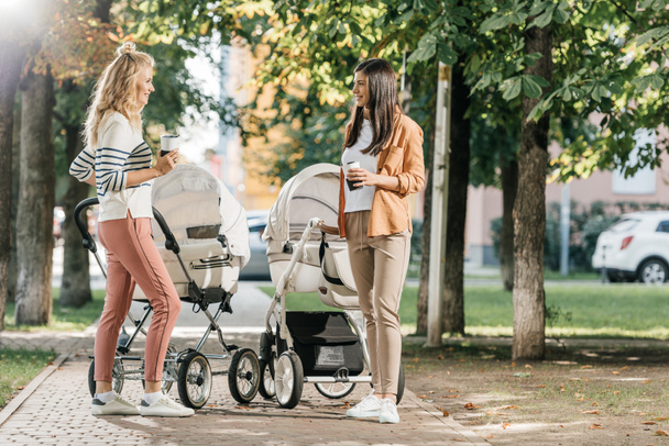 kahve ile ayakta anneler bebek arabasından Park yakınındaki gitmek  - Fotoğraf, Görsel