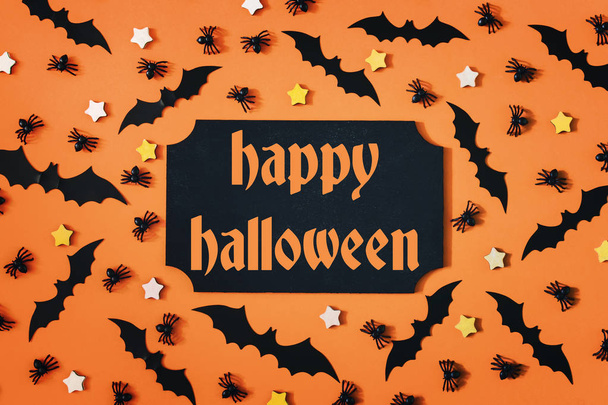 On an orange background, there are decorative bats, spiders and asterisks. Inscription in the center, Happy Halloween. Terrible picture for the holiday. - Photo, Image
