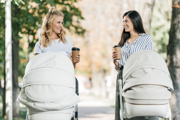 Glückliche Mütter spazieren mit Kinderwagen und Kaffee in Pappbechern im Park - Foto, Bild