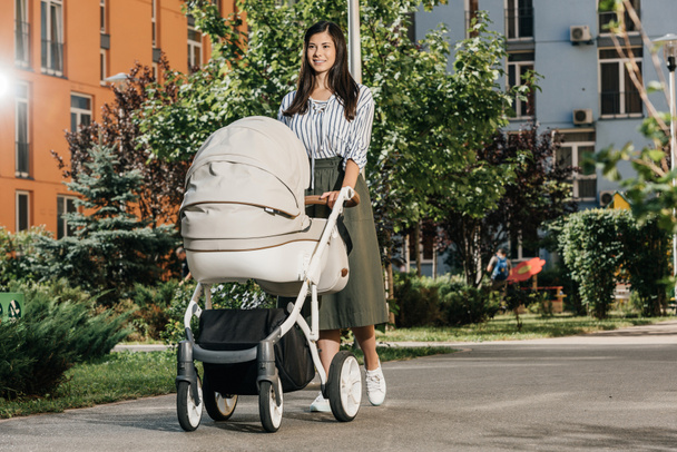beautiful brunette mother walking with baby stroller on street - Photo, Image