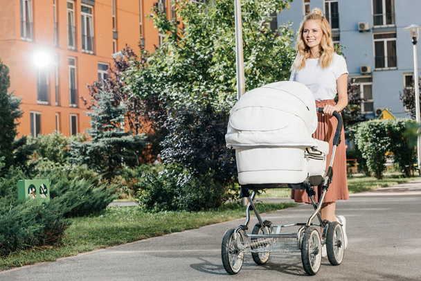 beautiful blonde mother walking with baby stroller on street - Zdjęcie, obraz
