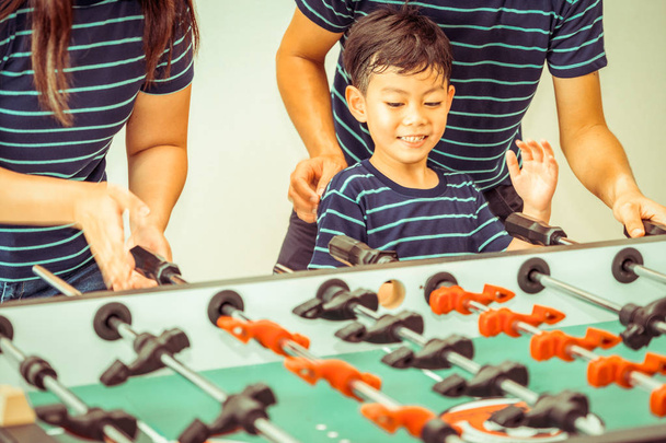 Happy kid playing foosball table soccer with family, father and mother. - Zdjęcie, obraz