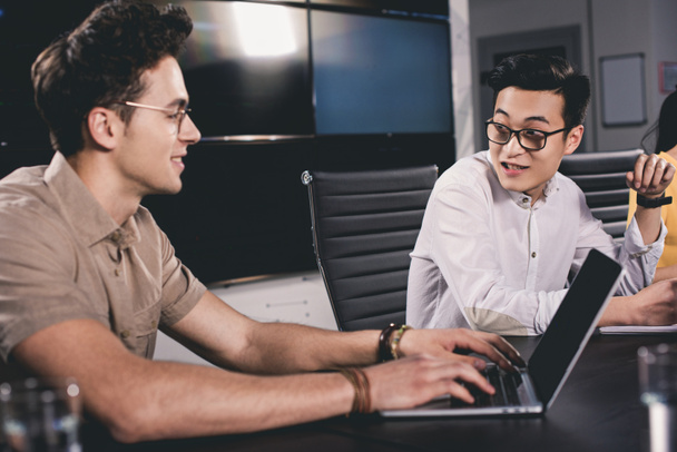 молодой азиатский бизнесмен разговаривает с коллегой во время использования ноутбука в современном офисе
  - Фото, изображение