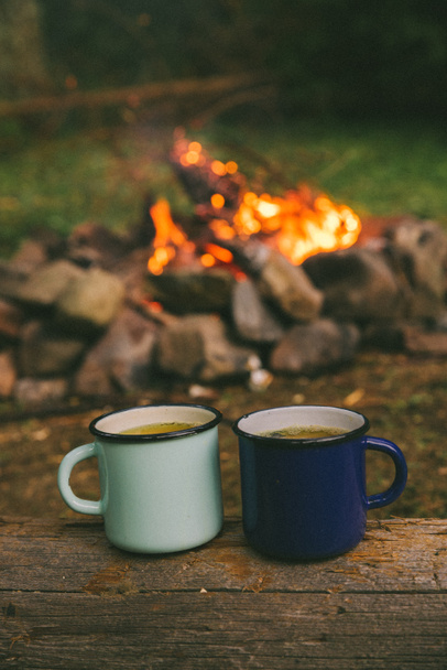 две металлические чашки с чаем. огонь на заднем плане. союз с природой
 - Фото, изображение
