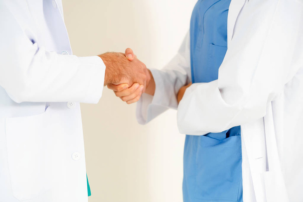 Médico de GP estrechan la mano con médico quirúrgico sobre fondo blanco
. - Foto, Imagen