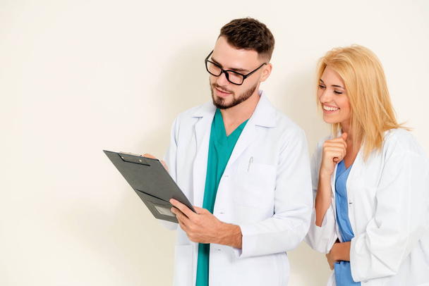 GP doctor looks at data in documents on clipboard while discussing with surgical doctor on white background. Medical service and healthcare concept. - Foto, Imagen