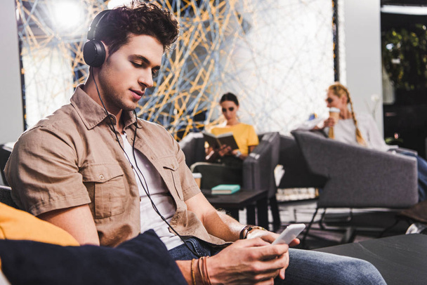 joven hombre de negocios en auriculares con teléfono inteligente en la moderna oficina de coworking
  - Foto, Imagen