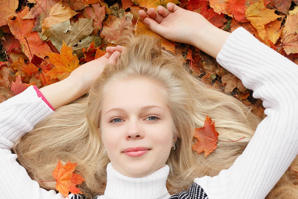 beauty, people, season and health concept - pretty girl is lying in yellow red Autumn leaves - Foto, afbeelding