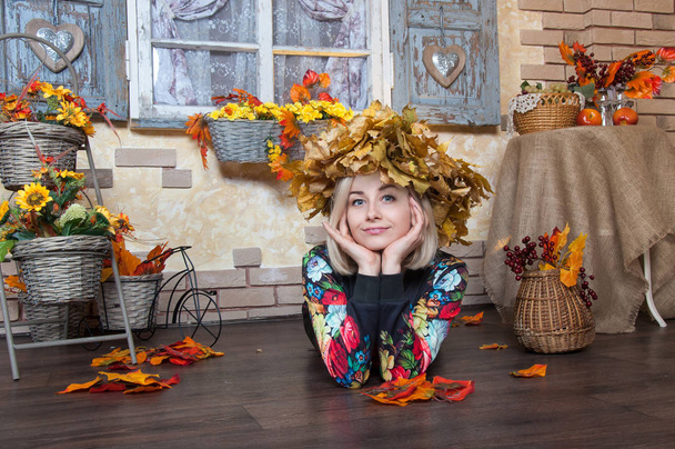 Autumn woman with autumn leaves. Cheerful young woman with autumn leafs. Girl wearing a wreath of yellow wilted leaves on her head at decorated home. Fall.  - Foto, Imagen