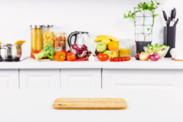 empty cutting board on table with ripe vegetables on background in light kitchen - Foto, imagen