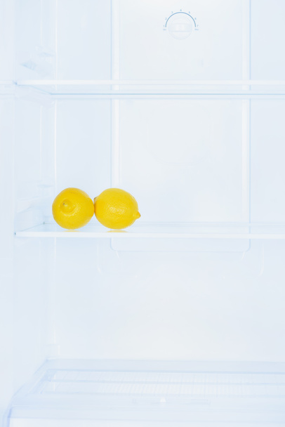 twee rijpe citroenen op plank in koelkast - Foto, afbeelding