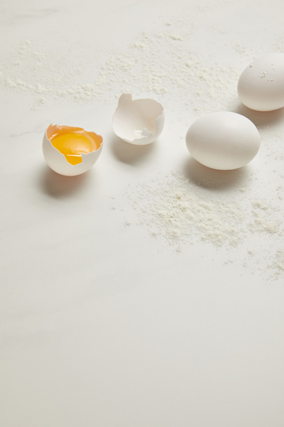 close up view of raw chicken eggs and flour on white marble tabletop - Фото, изображение
