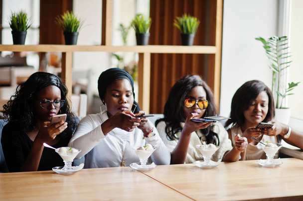 Four african american girls sitting on table at cafe with ice cream dessert and making food photo on phone. - Φωτογραφία, εικόνα