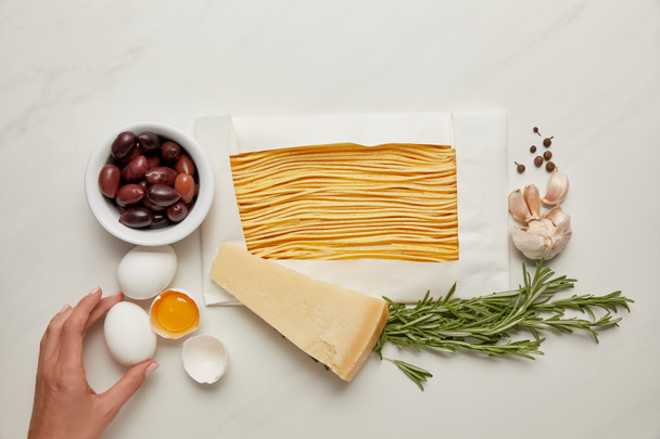 vista parcial de la mujer y los ingredientes de pasta italiana en la mesa de mármol blanco
 - Foto, Imagen