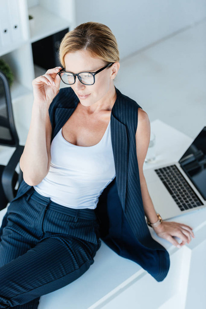 высокий угол обзора привлекательной деловой женщины, сидящей за столом с ноутбуком в офисе
  - Фото, изображение