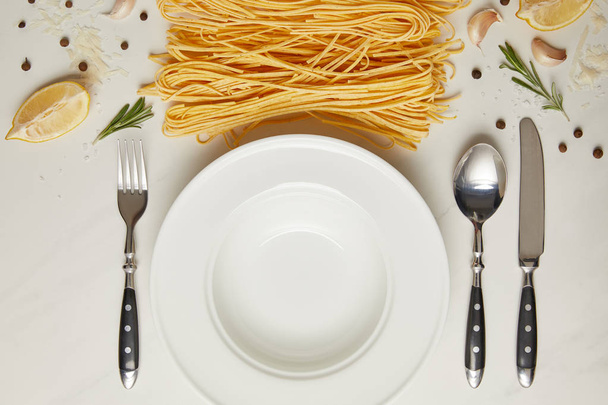 flat lay with empty plate and pasta ingredients on white marble surface - 写真・画像