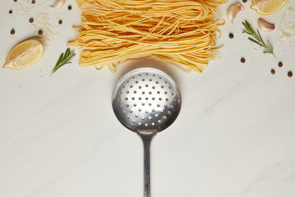 top view of ladle and italian pasta ingredients on white marble tabletop - Fotó, kép