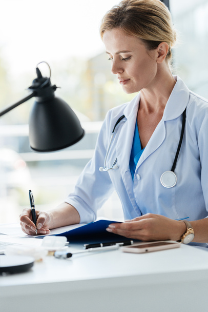 vertrouwen volwassen vrouwelijke arts in de witte jas met stethoscoop schrijven in Klembord aan tafel in kantoor  - Foto, afbeelding