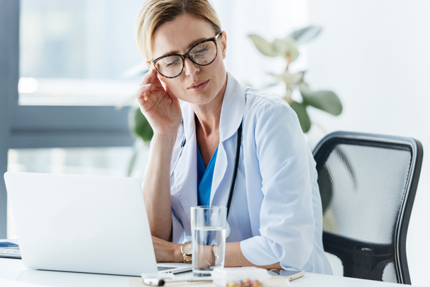 esausto medico femminile in occhiali con mal di testa a tavola in ufficio
  - Foto, immagini