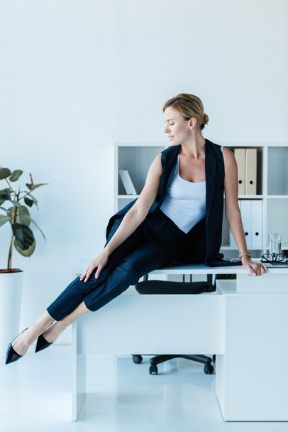 adult businesswoman looking away and posing on table in office  - Photo, Image