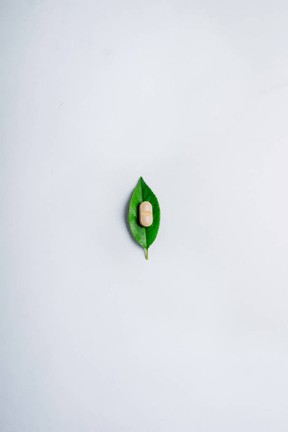 Одна таблетка з овочами на зеленому листі. Світлий фон, мінімалізм. Поняття альтернативної медицини
 - Фото, зображення