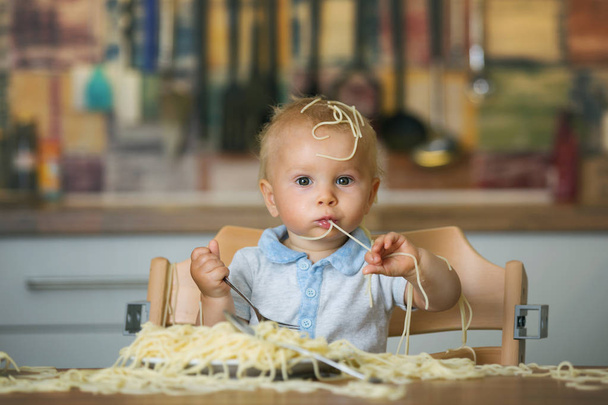Little baby boy, toddler child, eating spaghetti for lunch and making a mess at home in kitchen - Foto, immagini