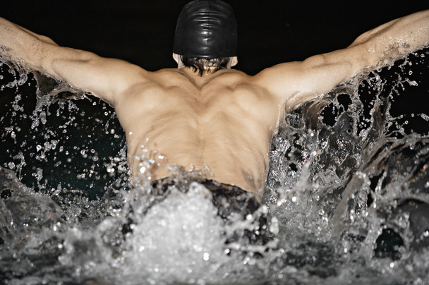Uros uimari tekee perhonen aivohalvauksia ja roiskuu vettä uima-altaassa
. - Valokuva, kuva