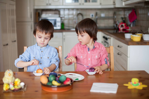 Two adorable boys, coloring eggs for Easter at home, having fun - 写真・画像