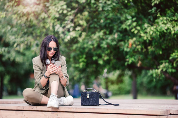 Aranyos nő olvas szöveges üzenetet a mobiltelefon, miközben ül a parkban. - Fotó, kép