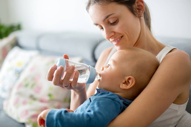 Mother, feeding her baby boy from bottle, comfortably sitting on the couch at home - Foto, Bild
