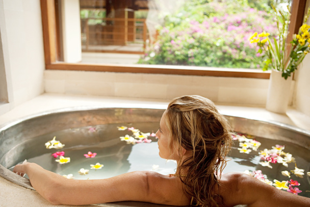 Vue arrière d'une jeune femme se baignant dans le bain de fleurs d'un spa de santé
. - Photo, image