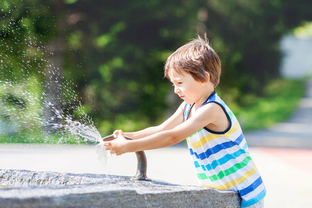 Sweet child, boy, splashing water from a fountain, happiness summertime - Foto, Imagen
