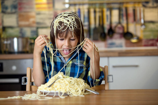 Little preschool boy, cute child, eating spaghetti for lunch and making a messat home in kitchen - Foto, imagen