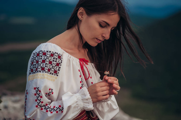 Atractive woman in traditional romanian costume on mountain green blurred background. Outdoor photo. Traditions and cultural diversity - 写真・画像