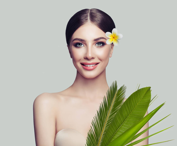 Wellness-Frau mit gesunder Haut, süßem Lächeln und tropischen Blättern und Blumen auf weißem Hintergrund, Wellness-Schönheit - Foto, Bild