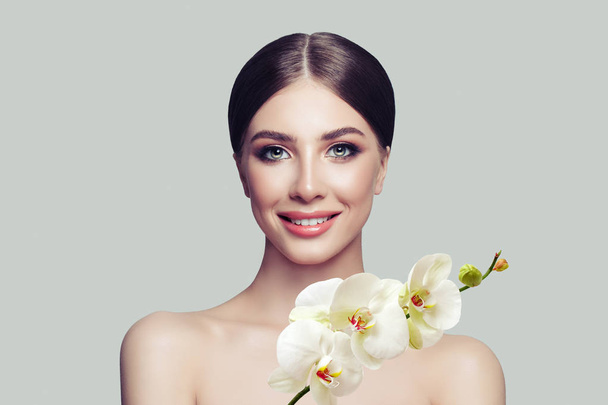 Happy woman spa model with healthy skin, cute smile and orchid flowers. Facial treatment, cosmetology, beauty salon, skin care and spa - Photo, image
