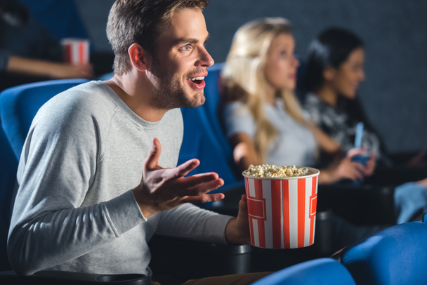 selective focus of emotional man with popcorn in cinema - Fotografie, Obrázek